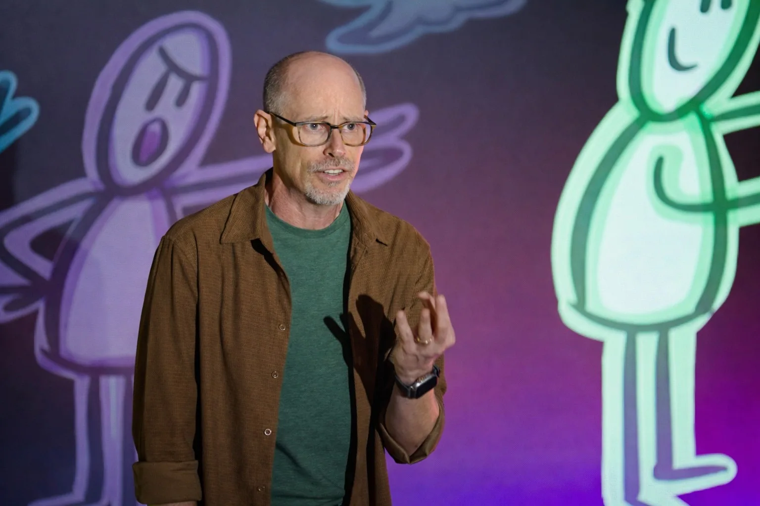 Eric McDermott speaking on stage, his hand-drawn figures projected on the screen behind him