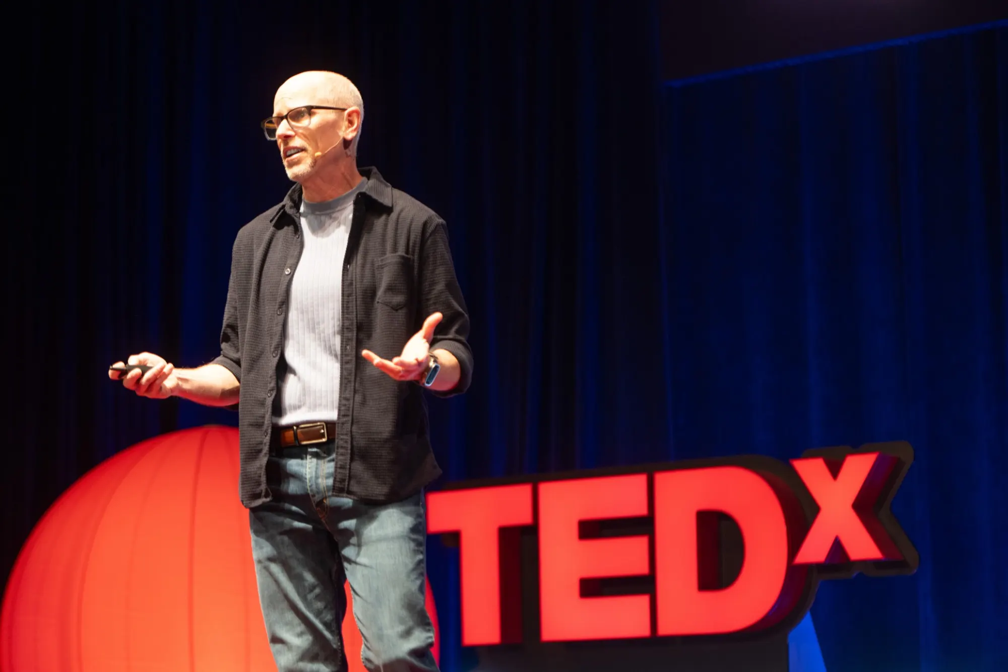 Eric McDermott on the TEDx stage, one hand open to the audience.