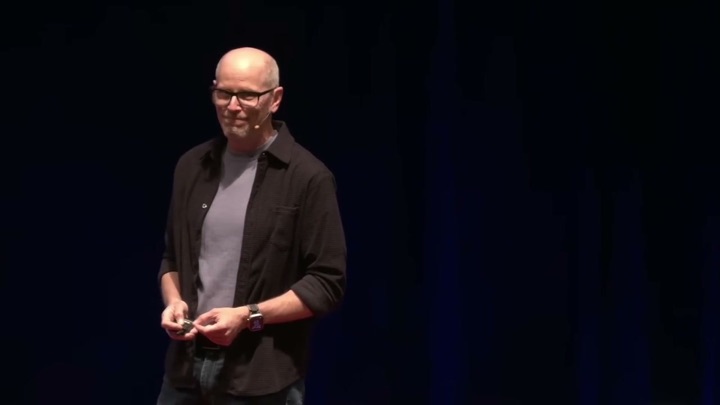 Eric McDermott smiling on stage, holding a slide clicker.