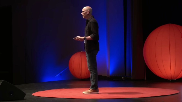 Eric McDermott speaking on the round red carpet at TEDx Sonoma County, red globe lights behind him.